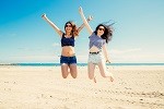 Happy and funny girl friends jumping on the beach, Some blur on legs beacuse of movement